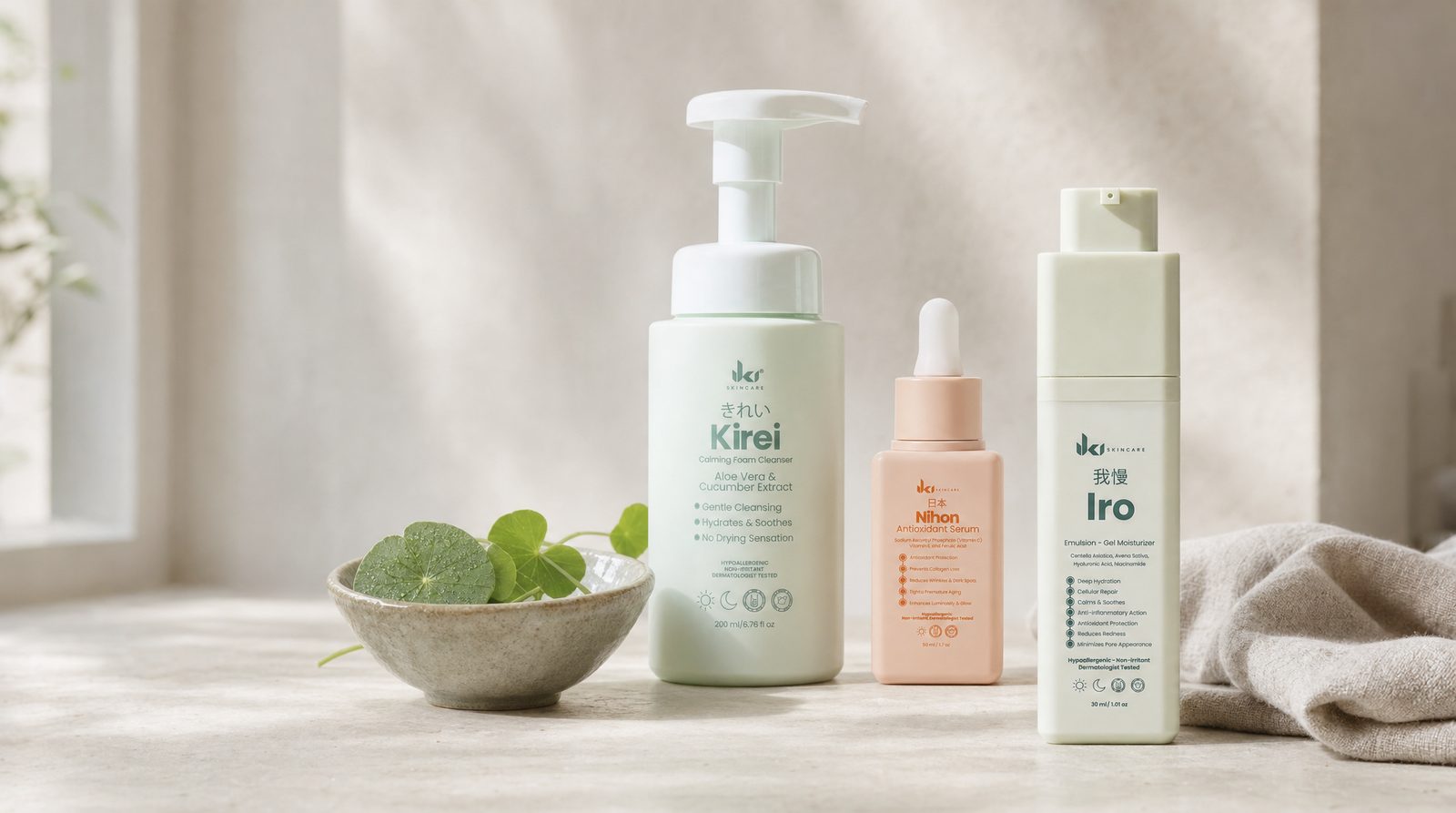 Rutina de mañana IKI para piel propensa a la rosácea: Kirei Calming Foam Cleanser, Nihon Antioxidant Serum e Iro Emulsion Gel Moisturizer sobre una superficie de piedra color crema junto a un tazón verde salvia con hojas de centella asiática